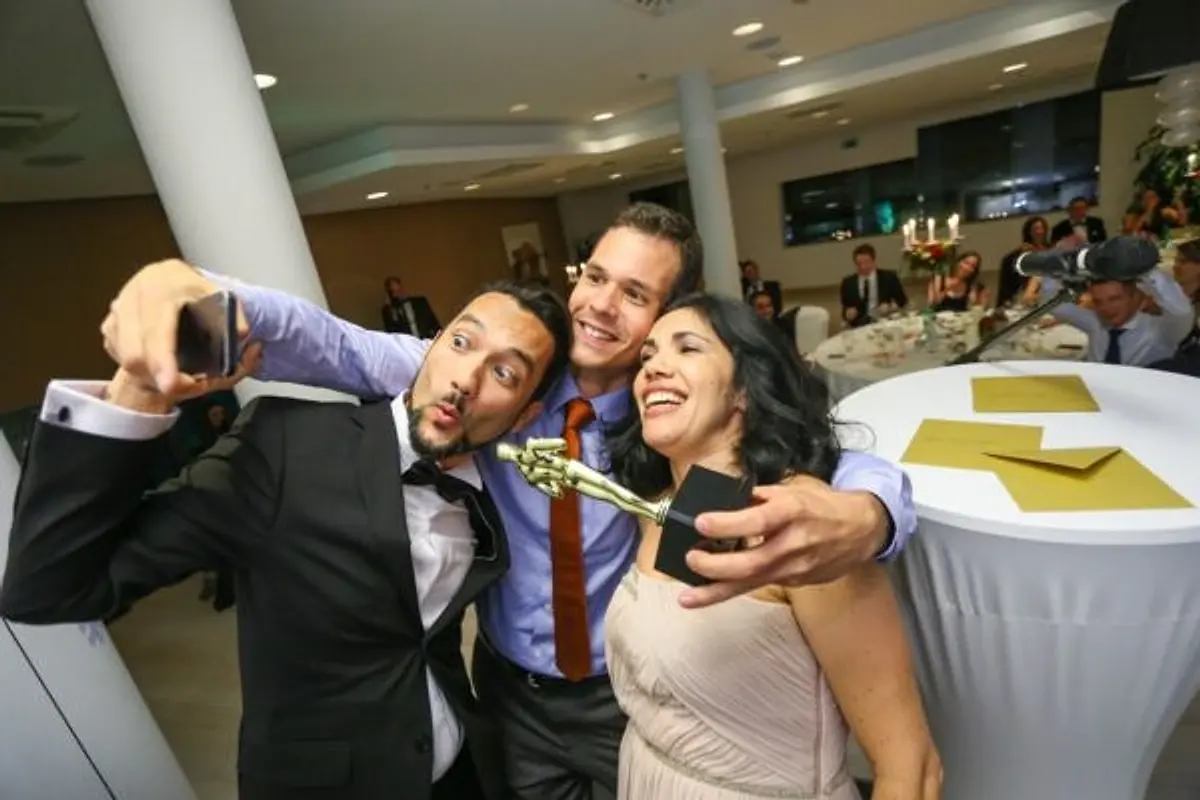 Three colleagues in evening wear taking a selfie with a golden statuette at a gala dinner