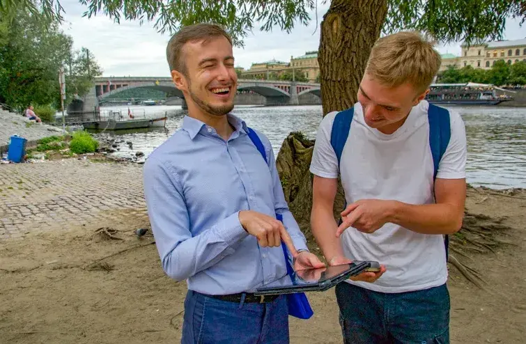 Two colleagues laughing as they solve a task on a tablet by the riverside